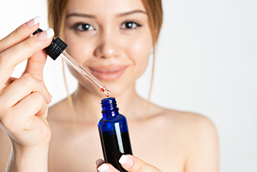 Caucasian female is holding a blue serum bottle in front of her face.