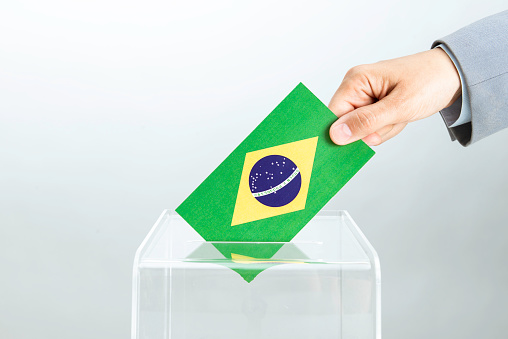 Human hand is inserting flag of Brazil into ballot box. Representing elections in Brazil concept.