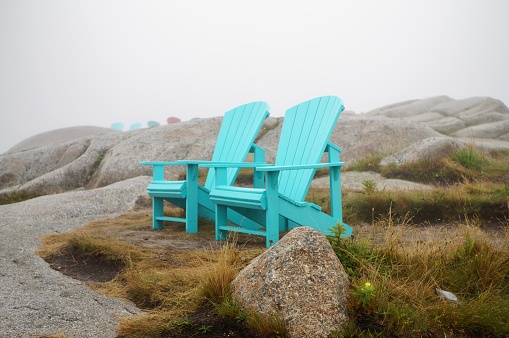 Two blue Muskoka chairs in the fog at Peggy’s Cove, Nova Scotia, Canada.