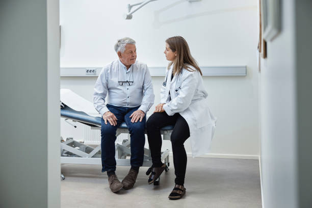 Mature patient talking to doctor while sitting on bed in clinic stock photo