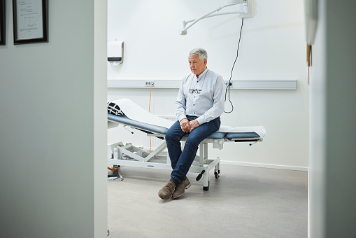 Senior male patient visiting a health care clinic. Elderly man sitting on examination table waiting for physician to start his treatment.