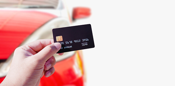 Hand holding credit card on blurred red car background, copy space, Online shopping and automotive concept