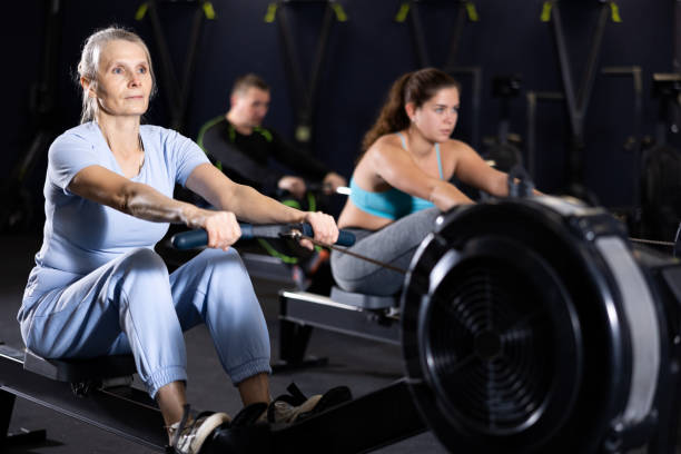 Senior woman working out on rowing machine in gym Concentrated sporty senior woman working out on rowing machine during total-body workout in gym. Active lifestyle of older adults concept senior bodybuilders stock pictures, royalty-free photos & images