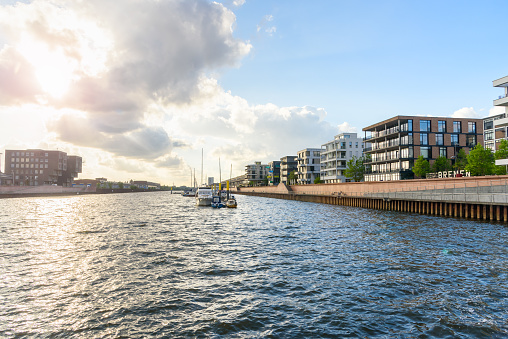 Modern apartment buildings in a redevelopped area along a former river harbour at sunset. Moored boats are visible in the middle of the harbour. Bremen, Germany.
