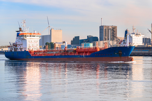 Chemical tanker leaving a commercial port at sunset. Docks, factories and wind turbines are in background. Rotterdam, Netherlands.