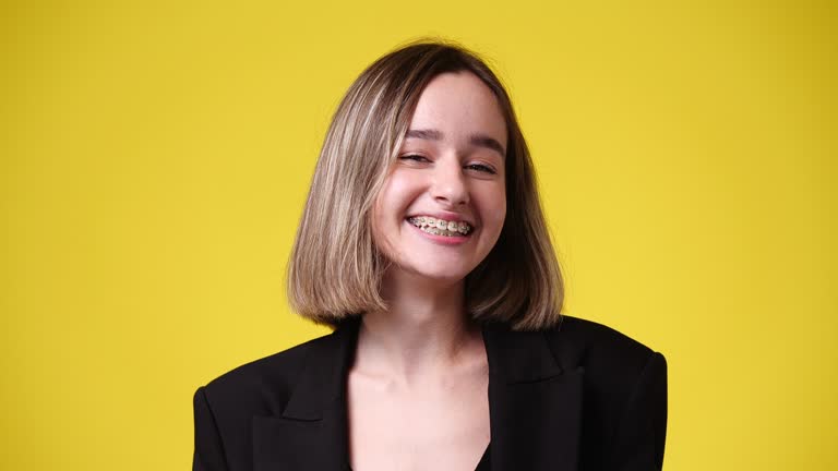 4k video of one girl points his finger at the braces and smiles over yellow background.