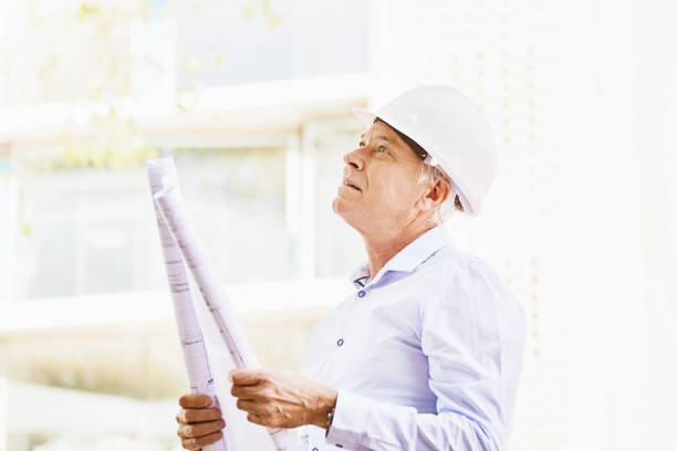 Handsome mature man wearing protective construction helmet, holding plans. Copy space on the bright sunlit background.
