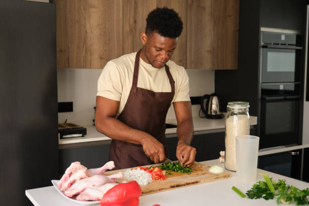 Young african man cutting celery to prepare chicken recipe.