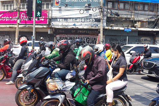 Waiting thai people on motorcycles using mobile phones captured at junction Asoke Rd and Phetchaburi Rd. in Bangkok. Most people are wearing crash helmets. Many are using mobile phones both drivers and co-drivers in back