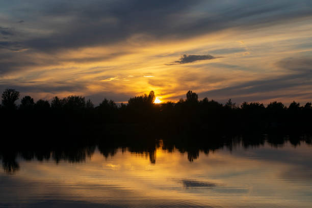 Infernal sunset behind trees and reflection in water. stock photo