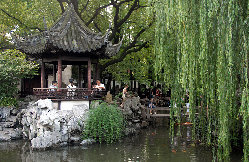 Yu Yuan Garden in the Old Town of Shanghai, China. A traditional Chinese garden with trees, rocks and water. People sit in a pavilion, others explore