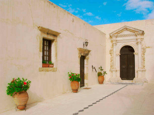 Greece, Crete. Inner courtyard of the Gonia Monastery (other name is Monastery of Panagia Odigitria) with flower floor pots and ornate decorated portico with a door.