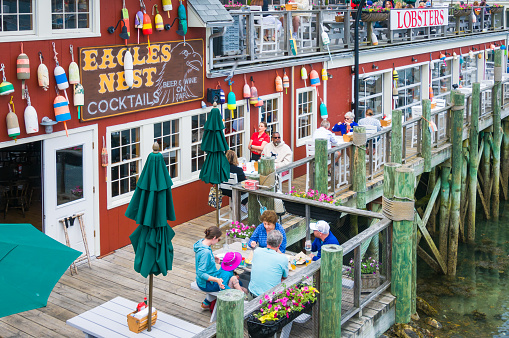 Bar Harbor, Maine, USA- May 26, 2022-  Tourists enjoy a meal of fresh seafood on the narrow outside deck of the Eagles Nest restaurant situated on a dock overlooking Bar Harbor
