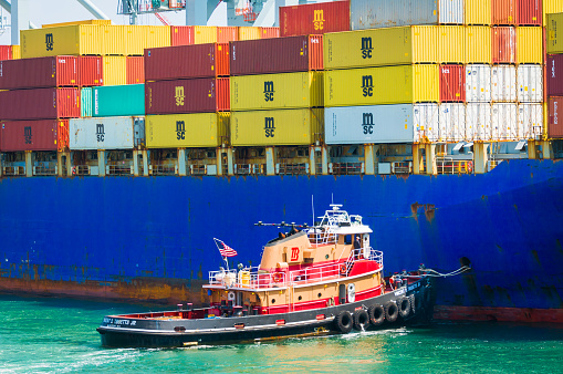 Boston, Massachusetts, USA -May 20, 2022-  The tugboat Vincent D. Tibbitts, Jr nudges the side of a large container ship into a secure docking position in the busy Port of Boston