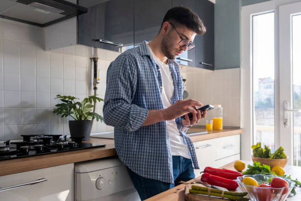 istock Young adult man looking at phone in kitchen 1469793735