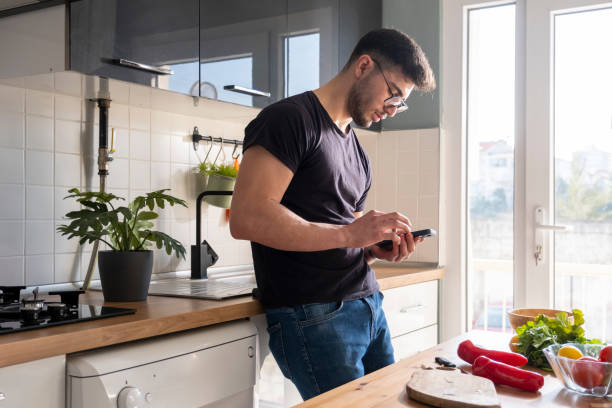 istock Young adult man looking at phone in kitchen 1469793737