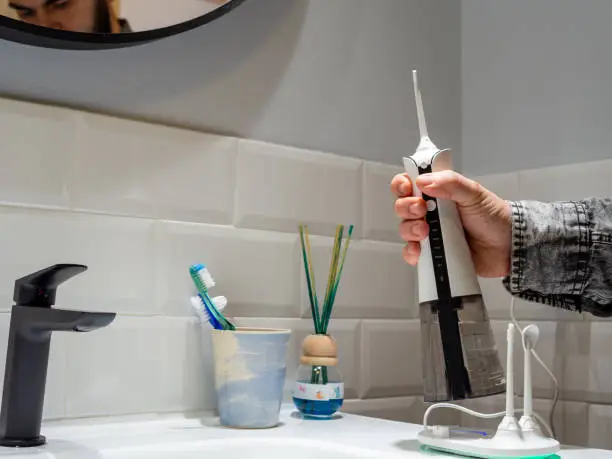 young man holding a domestic wireless dental water flosser on the bathroom wash basin