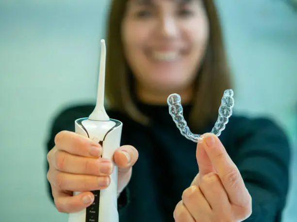 Maintaining a healthy smile: a young woman performs her dental hygiene routine at home using a domestic dental water flosser and her dental aligner.