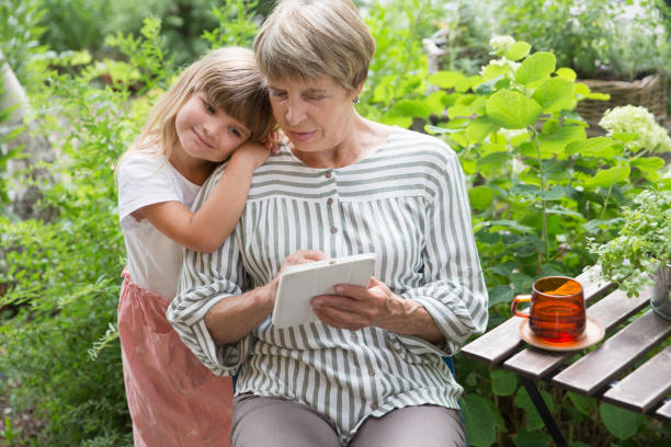 grandmother and little granddaughte using tablet and having fun together in the garden. Happy family enjoying summer outdoors. stock photo