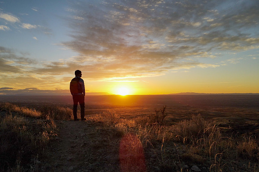 a solo man makes his way across the beautiful landscape underneath a sunset sky at golden hour.