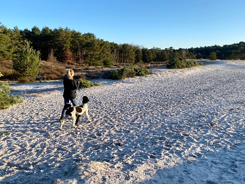 Brunssum, Netherlands - February 23, 2023. Woman walking with her dog on a cold Sunday in the heat area cold Brunssummerheide.