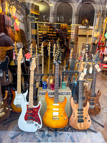 Beyoglu, Istanbul, Turkiye - January 19, 2023: Many musical equipment are displayed inside a store. Various bass electro guitar string instruments. Reflection on window.