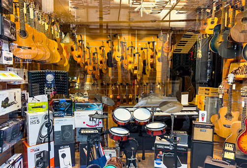 Beyoglu, Istanbul, Turkiye - January 19, 2023:  Many musical equipment hanging on the ceiling and displayed inside a store. Various string instruments: guitar, viola, lute or the traditional saz or baglama (turkish names). Reflection on window.