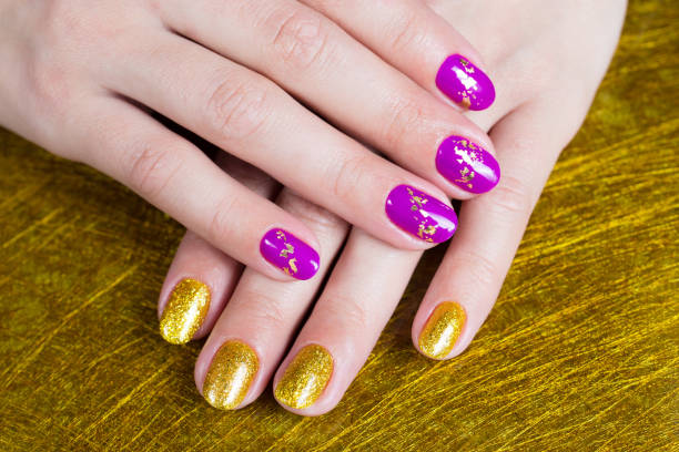 Female hands with a gold and purple colour nails. Nail design. Artistic manicure with gel polish stock photo
