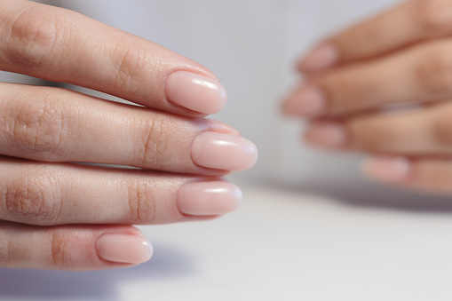 Hands of a young woman with a gentle nude manicure on her nails. Classic bridal nail design.