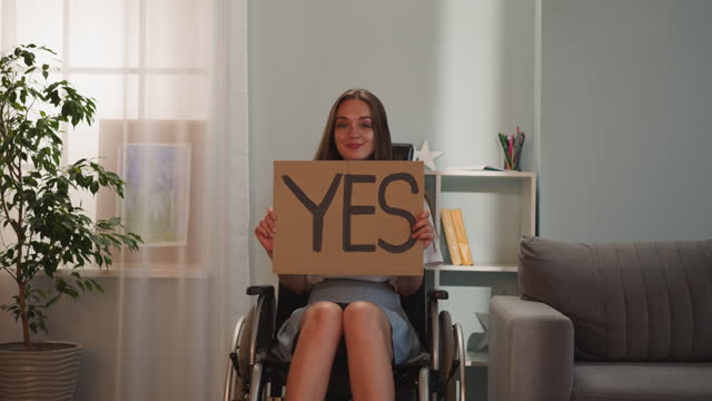Cheerful disabled woman turns poster with word Yes to camera