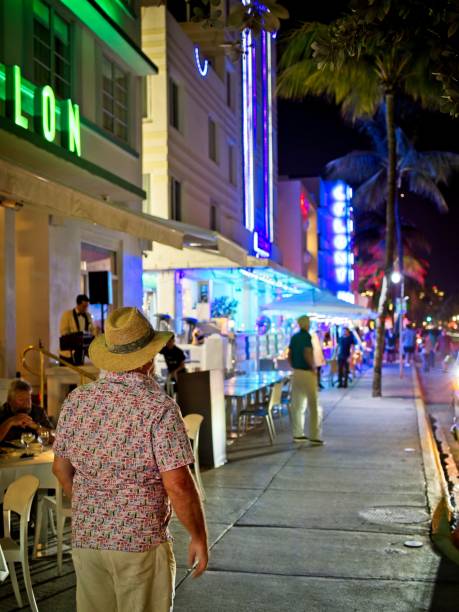 Gentleman looks down Ocean drive at the dazzling array of brightly lit signs in the heart of the Miami art deco district Miami Beach FL - USA, February 1, 2023. Gentleman looks down Ocean drive at the dazzling array of brightly lit signs in the heart of the Miami art deco district. 1 hotel south beach stock pictures, royalty-free photos & images