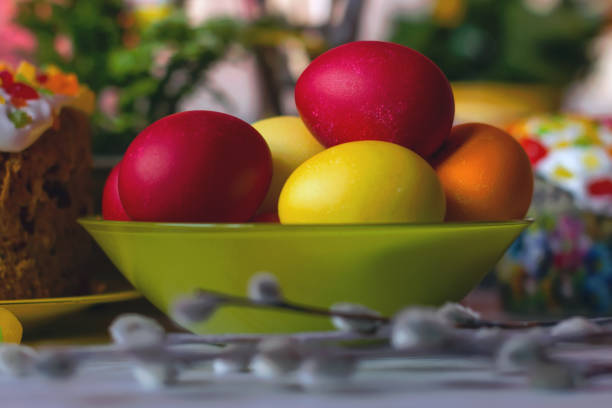 Painted Easter eggs in a green glass bowl on a wooden table stock photo