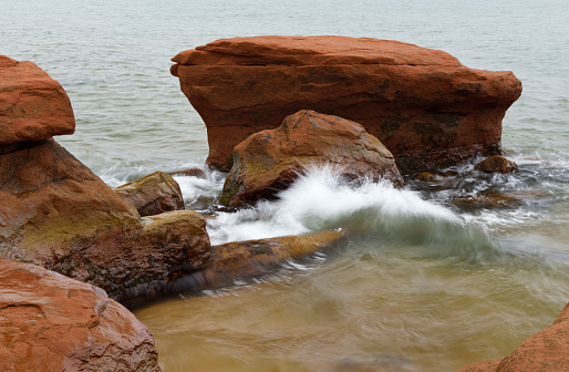 Eroded coastal red rocks and wave, Magdalen Islands, Quebec