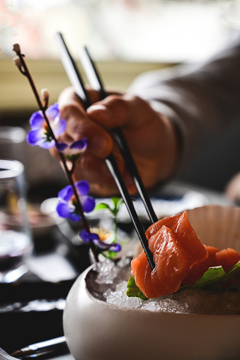 close up of a man eating salmon sashimi in a sushi bar.