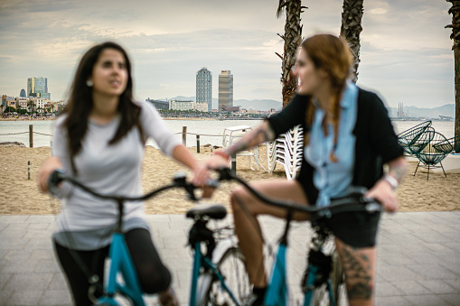 Two friends in Barcelona at summer. The women go around Barceloneta with bicycles