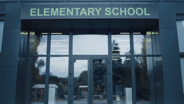 Elementary school exterior outside with closed door. Window reflecting sky trees