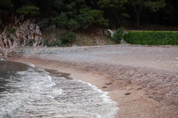 Photo of Royal Beach with small pebbles in Montenegro. The tide of the sea on the shore. Green forest