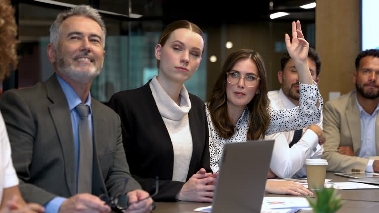 Group of people listening to a presentation. One person has their hand raised asking or answering a question.