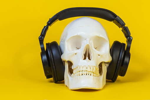 human skull in headphones, skeleton bone,headphones for listening to music,object,funny ,scary,listening to music stands on the surface of yellow background. concept music copyright infringement