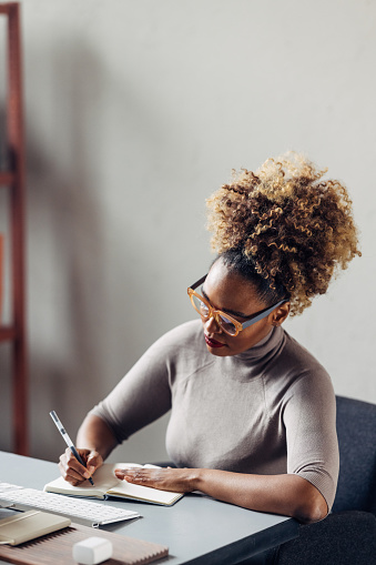 A smiling African-American entrepreneur with glasses  making some business plans while sitting at the desk in her office.