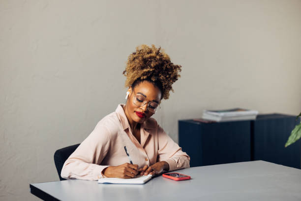 istock A Happy Beautiful Businesswoman With Blonde Curly Hair Taking Some Notes While Using Her Earbuds And Mobile Phone 1469817381