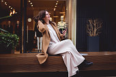 Fashionable woman in a brown trendy wool coat  sitting outdoors while having a break from a work in office.