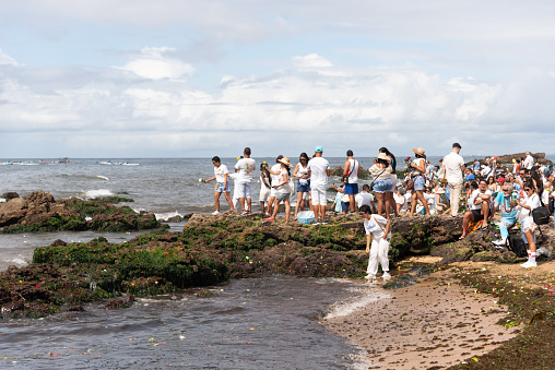 Salvador, Bahia, Brazil - February 02, 2023: People are seen on top of the rocks at Rio Vermelho beach, offering gifts to Yemanja, in Salvador, Bahia.