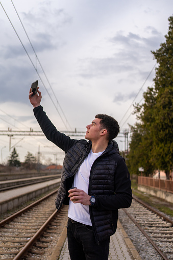 Young man takes a picture of himself at a train station while waiting a train.
