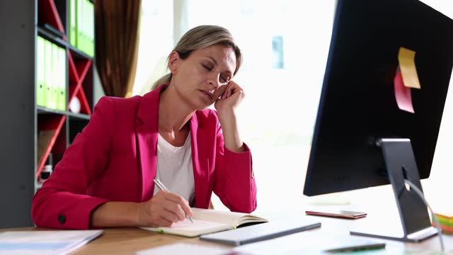 Tired woman sits at computer screen and holds head and falls asleep