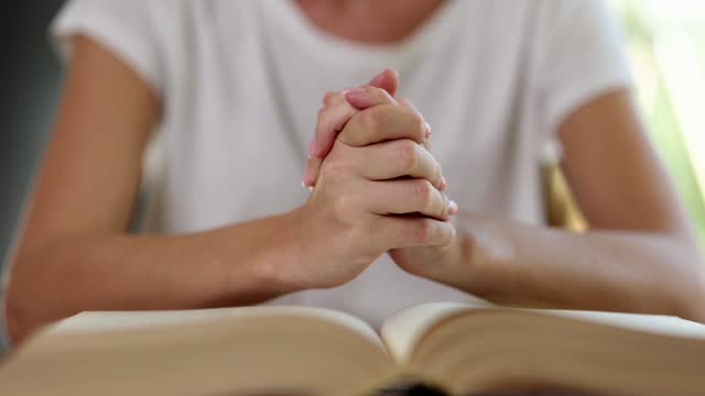 Female hands with open bible book and keeps hands together on book pages