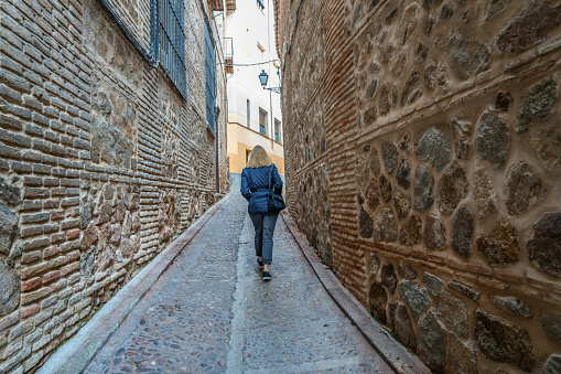 Blond woman walking the quiet alleys of old town Toledo Spain on a winter day
