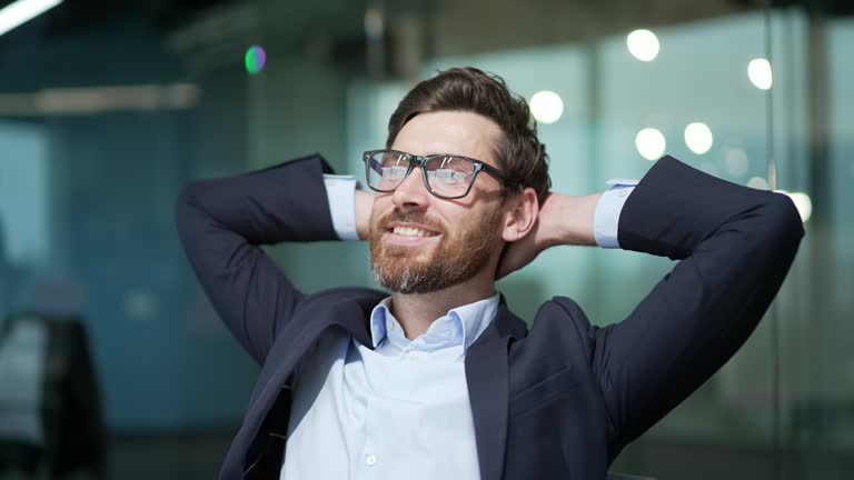 Resting entrepreneur investor with hands behind head feels satisfied with work well done indoor Calm bearded businessman relax after hard working day