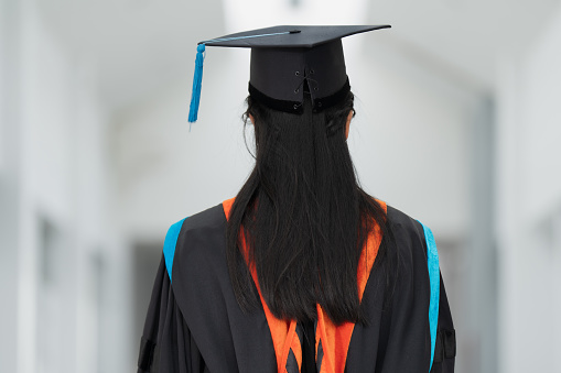 Rear view of a young Asian woman university graduate in graduation gown and cap