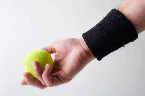 Background with hand with black wristband catching tennis ball on light isolated background. Front view.